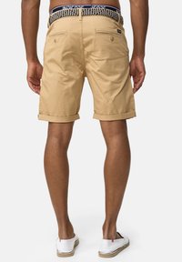 Shorts beiges avec un ourlet replié, dotés de deux poches arrière et d'une ceinture en tissu à motifs bleu marine. Tissu doux et tissé avec une texture lisse.