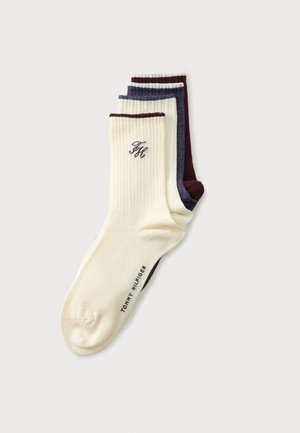 Trois paires de chaussettes côtelées montantes empilées, en crème avec bord foncé, bleu foncé avec des taches blanches, et rouge foncé, avec le branding Tommy Hilfiger.