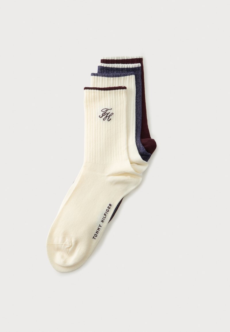 Trois paires de chaussettes côtelées montantes empilées, en crème avec bord foncé, bleu foncé avec des taches blanches, et rouge foncé, avec le branding Tommy Hilfiger.