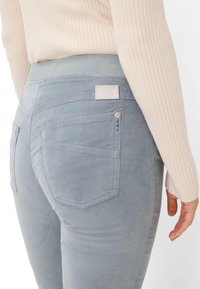 Grijze corduroy broek met een zachte textuur, voorzien van een achterzak met stiksels en een label. De tailleband is elastisch en glad.