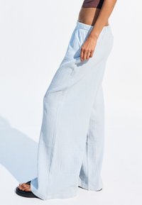 Pantalons larges bleu clair en tissu texturé avec une taille élastique, offrant une coupe décontractée et sans quincaillerie visible.