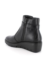 Stivaletto in pelle nera con zip laterale, suola a zeppa bassa e dettagli di cucitura, mostrato dal lato esterno su uno sfondo bianco.