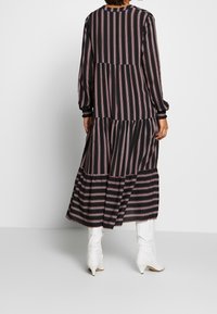 Černé a růžové pruhované šaty s volány a dlouhými rukávy, s kulatým výstřihem, vyrobené z texturované tkaniny a s elastickými manžetami. Nosené s bílými kotníkovými botami.