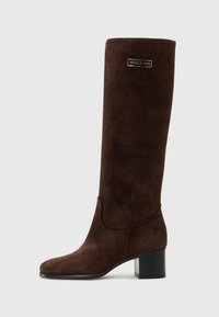 Stivale marrone in suede fino al ginocchio con silhouette dritta, tacco a blocco e accentuazione del logo vicino alla parte superiore. Texture liscia con punta rotonda.