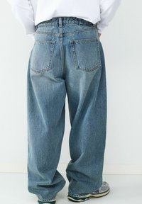 Weit geschnittene blaue Jeans aus Denim mit verwaschenem Look, ausgestattet mit zwei Gesäßtaschen und einem hohen Bund. Das Material hat eine glatte, strukturierte Oberfläche.