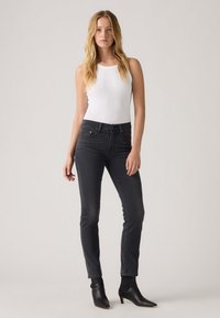 Vaqueros negros de talle alto con corte ajustado, cinco bolsillos y trabillas para cinturón. Combinados con una blusa blanca sin mangas y botines negros de punta.