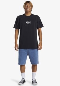 Black cotton t-shirt with a round neckline and a small, white logo on the chest, paired with blue denim shorts and black sneakers.
