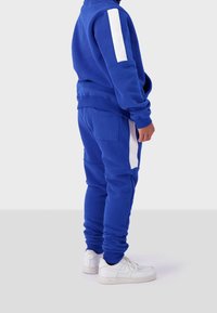 Blue sweatshirt and matching joggers with white side stripes, made from soft fabric. Features relaxed fit, ribbed cuffs, and side pockets.