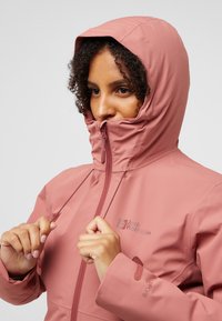 Roze waterdichte jacket met capuchon, frontale rits en verstelbare koord. Beschikt over een logo op de borst en elastische manchetten voor een goede pasvorm.