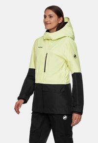 Wasserdichte Jacke mit einem leuchtend gelben Oberteil und einem schwarzen unteren Abschnitt. Verfügt über eine Kapuze, einen Frontreißverschluss und ein Logo-Detail am Ärmel.