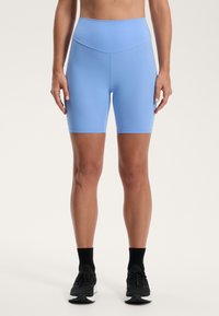 Svijetloplave biciklističke šorts hlače visokog struka izrađene od rastezljivog materijala, s glatkom teksturom i uskim dizajnom, u kombinaciji s crnim sportskim cipelama.
