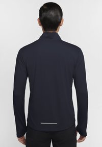 Camisetta a maniche lunghe, traspirante e ad asciugatura rapida, di colore blu scuro con un motivo discreto, colletto alto e accenti riflettenti vicino all'orlo.