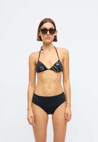 Μαύρο μπικίνι σετ με τριγωνικό τοπ με μοτίβο και ψηλόμεσο κάτω μέρος. Συνοδεύεται από μαύρα γωνιακά γυαλιά ηλίου.
