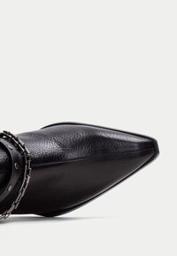 Botín negro de cuero hasta el tobillo con un diseño de punta afilada, que presenta un detalle de cadena alrededor del puño y un acabado suave y texturizado.