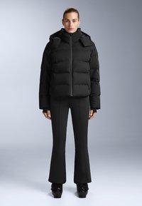 Fekete puffdzseki magas gallérral, cipzáros elejével és széles panelekkel. Fekete harangnadrággal és platform cipőkkel párosítva. Simább anyagtextúrával.