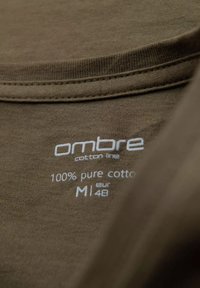 Hnědá bavlněná tričkovina s hladkou texturou. Má štítek s nápisem "ombre cotton line 100 % čistá bavlna M1 48" a pokyny k údržbě.