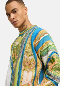 Kolorowy dzianinowy sweter z misternymi wzorami w odcieniach niebieskiego, zielonego, pomarańczowego i żółtego. Teksturowana tkanina o luźnym kroju i dekolcie typu crew neck.
