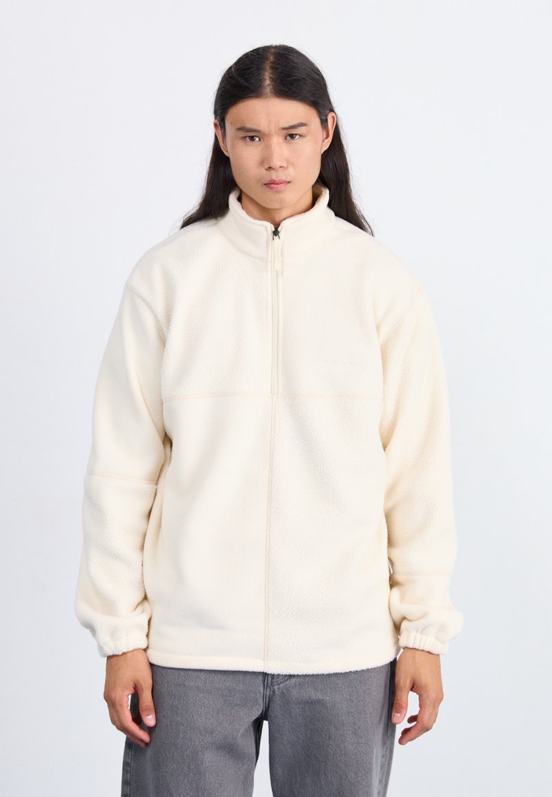 Karamelli fleece takki, jossa on korkea kaulus, puolivälin vetoketju ja elastiset hihat, sekä sileä pinta ja minimalistinen muotoilu.