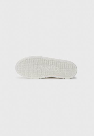 Sole of a white sneaker with textured tread pattern and raised brand logo "VERSACE" embossed in the center.