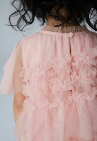 Roza obleka iz tila z večplastnimi volani, kratkimi rokavi in zapenjanjem na hrbtu. Vključuje podložen trup in teksturirano, prozorno tkanino.