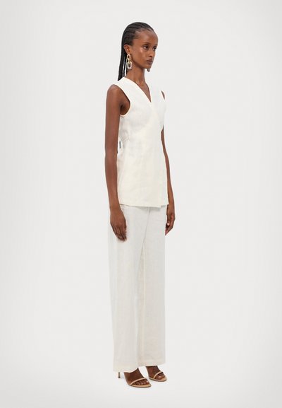 Top sans manches en lin blanc cassé avec un décolleté en V et un design cache-cœur, associé à un pantalon léger et ample et des sandales à bout ouvert.