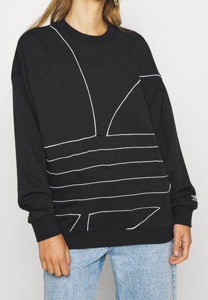 Schwarzes Sweatshirt mit langen Ärmeln und weißen abstrakten Linienmustern, kombiniert mit hellblauen Jeans, getragen von einer stehenden Person mit teilweiser Ansicht.