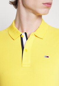 Gul polo skjorta tillverkad av texturerad tyg med klassisk krage, som har en tvåknapplåsning och en logotyp på bröstet.