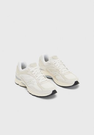 Para kremowych sportowych sneakersów z siateczką i skórzanymi detalami, białymi sznurowadłami i czarną podeszwą, prezentowanych na jednolitym jasnym tle.