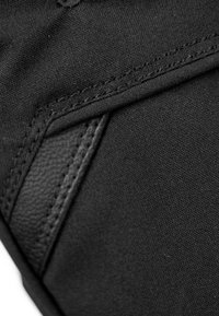 Schwarzer Stoff mit glatter Textur, der durch detaillierte Nähte und einen Ledereinsatz hervorgehoben wird und die strukturellen Designelemente des Kleidungsstücks betont.