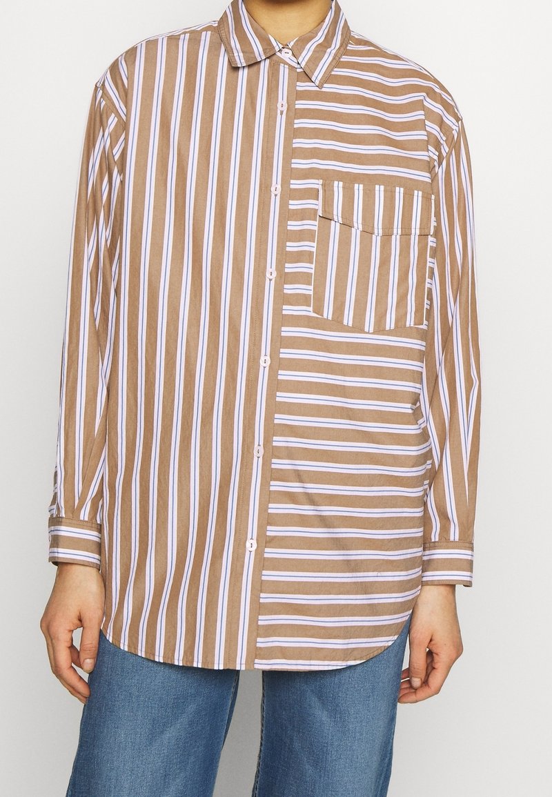 Chemise boutonnée avec des rayures verticales marron et blanches d'un côté et des rayures horizontales de l'autre, associée à un jean bleu.