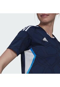 Maglietta atletica a maniche corte di colore blu navy con texture geometrica, dettagli in mesh bianco e bordature blu. Include tre strisce bianche sulla spalla.