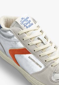 Srebrne i kremowe sneakersy z pomarańczowym akcentem, teksturowane materiały, beżowe sznurówki oraz etykieta marki na języku. Wysoka cholewka z zamszu.