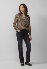 Blouse semi-transparente à motif léopard avec col et fermeture à boutons, associée à un jean en denim foncé et des chaussures plates noires.