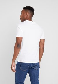 Hvid bomulds t-shirt med rund hals og korte ærmer, parret med blå denim jeans, set fra ryggen. Renset og enkel design.