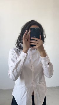 White button-up shirt with long sleeves, featuring a soft, textured fabric and a slight sheen. The shirt has a curved hem and classic collar.