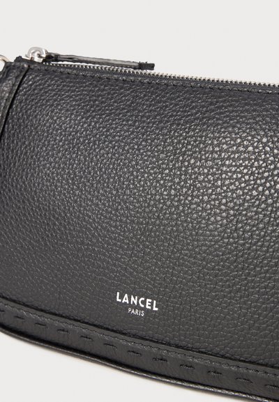 Черна текстурирана кожена чанта с цип и бял логотип "LANCEL PARIS" отпечатан на предната част.