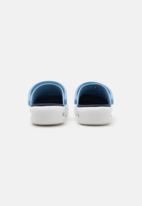 Light blue clogs with a perforated upper and white sole, featuring a back strap and interior cushioning for comfort.