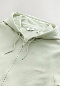 Világos zöld, cipzáros kapucnis pulóver, puha anyagból készült, állítható kapucnival, bordás mandzsettákkal és letisztult, egyszerű dizájnnal.