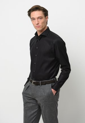 Zwart shirt met lange mouwen en een fitted ontwerp, met knopen aan de voorkant, gedragen met grijskleurige, gestructureerde broek en een leren riem in het bruin, op een model tegen een witte achtergrond.