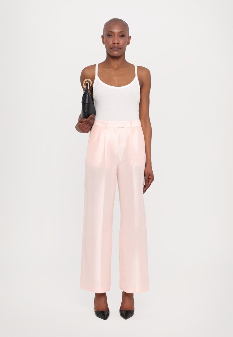 Pantalones de tiro alto en rosa claro, con una textura suave y un diseño de pierna ancha. Combinados con una camiseta sin mangas ajustada blanca y un bolso negro.