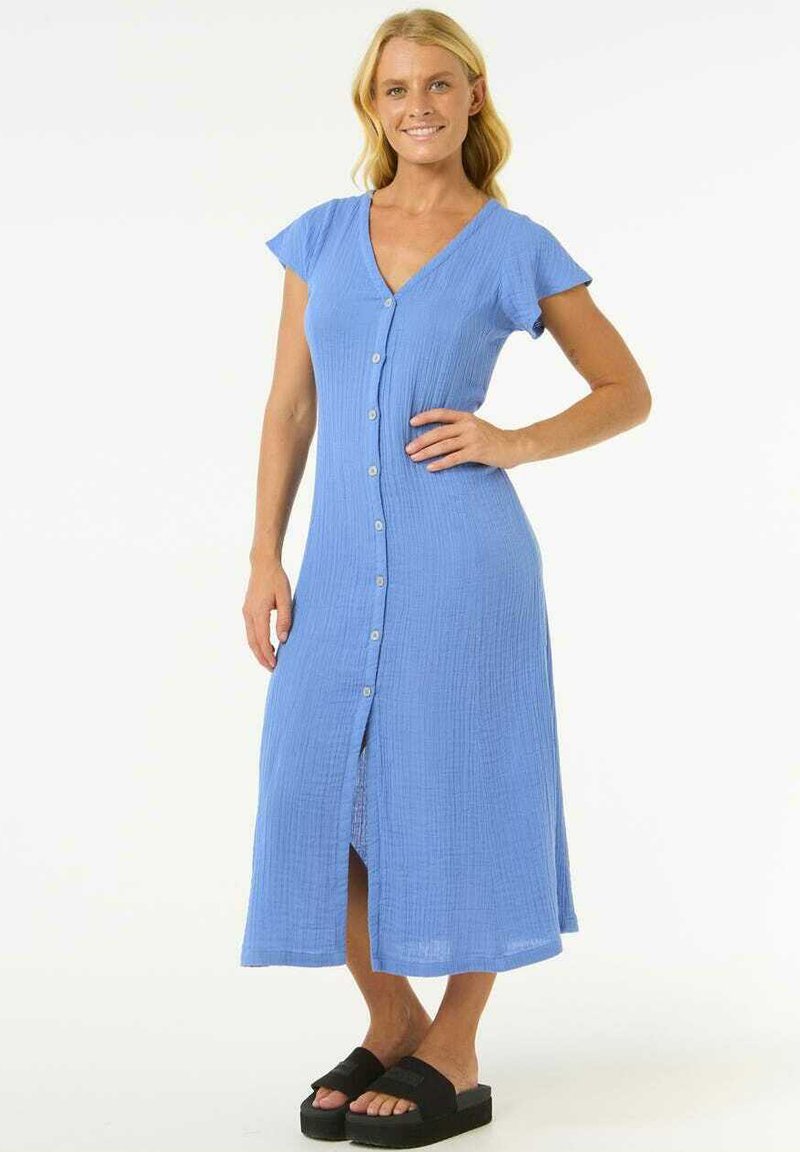 Robe chemise bleu clair à manches courtes, longueur genou, en tissu texturé, avec une fente sur le devant; portée avec des sandales à plateforme noires.