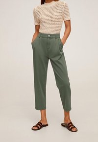 Lichtbeige gebreid topje met korte mouwen, gecombineerd met hoge taille, rechte groene broek. Bruine schuifsandalen maken de outfit compleet.