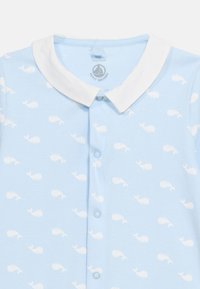 Φωτεινό γαλάζιο βρεφικό φορμάκι με λευκή γιακαδάκι, κουμπιά ασφαλείας και μοτίβο από μικρά λευκά φάλαινες σε όλο το σχέδιο. Μέγεθος 12 μηνών.