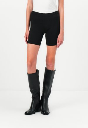 Black stretchy bike shorts with a fitted design, paired with tall black leather heeled boots featuring side zippers and textured surface.