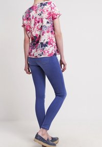 Top à manches courtes fleuri avec des motifs roses, blancs et navy. Associé à un jean skinny bleu et des chaussures en toile navy à enfiler. Texture de tissu lisse.