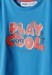 Modrá bavlněná tričko s odvážným, barevným grafickým textem "HRÁJ COOL VŽDY," s ilustrovanými akcenty rukou a brýlí.