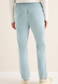 Pantaloni azzurri chiari con elastico in vita, dal taglio affusolato e due tasche posteriori, abbinati a sneakers di colore chiaro. Texture morbida e liscia.