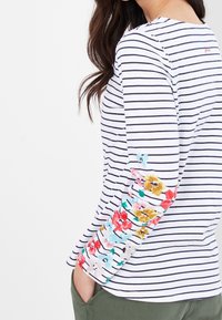 Randig långärmad skjorta i vitt och marinblått med blommotiv på ärmarna. Har rundad halsringning och en avslappnad passform.