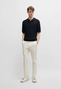 Polo a maniche corte blu navy con motivo testurizzato, abbinato a pantaloni crema e sneakers bianche. Design semplice e moderno.