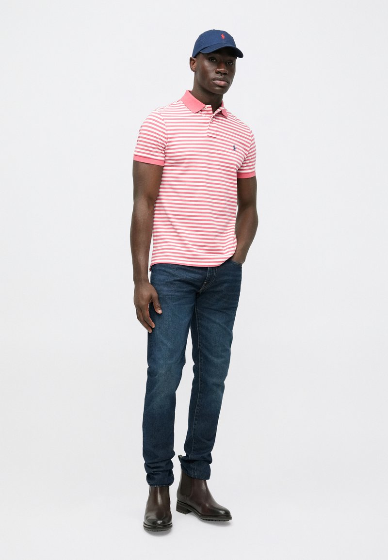 Short-sleeve polo shirt in red and white stripes, with a contrasting pink collar, paired with dark blue jeans and brown ankle boots.